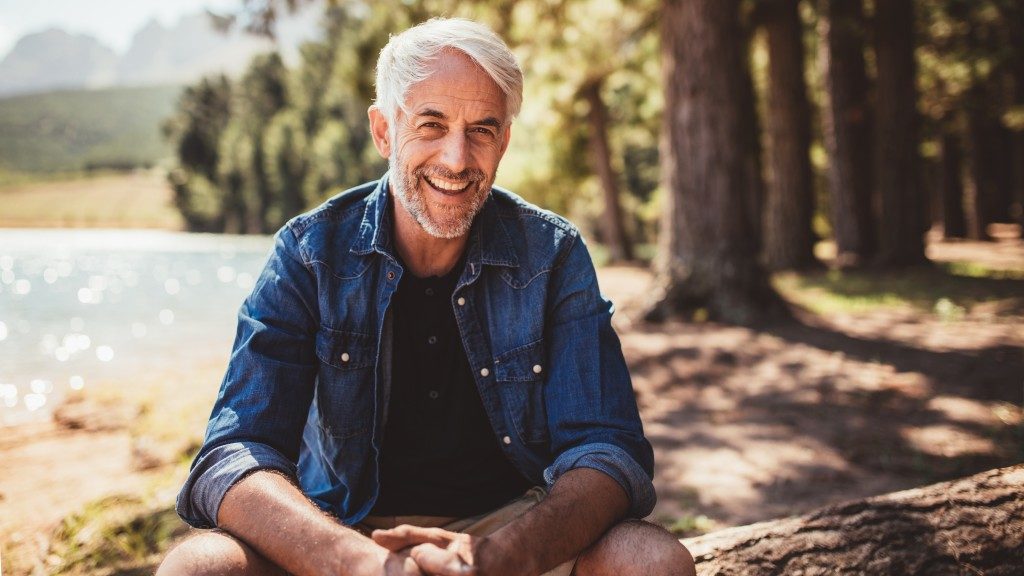 Mature man smiling while sitting beside the lake