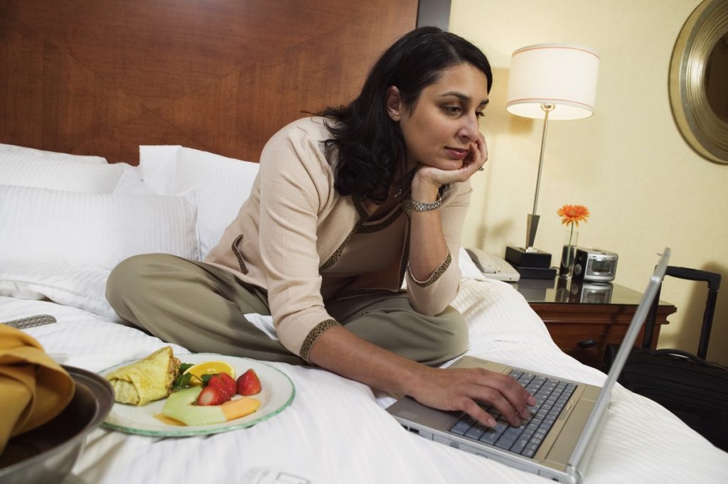 woman using laptop on hotel bed