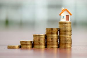 stacks of gold coins with miniature felt house in the highest stack